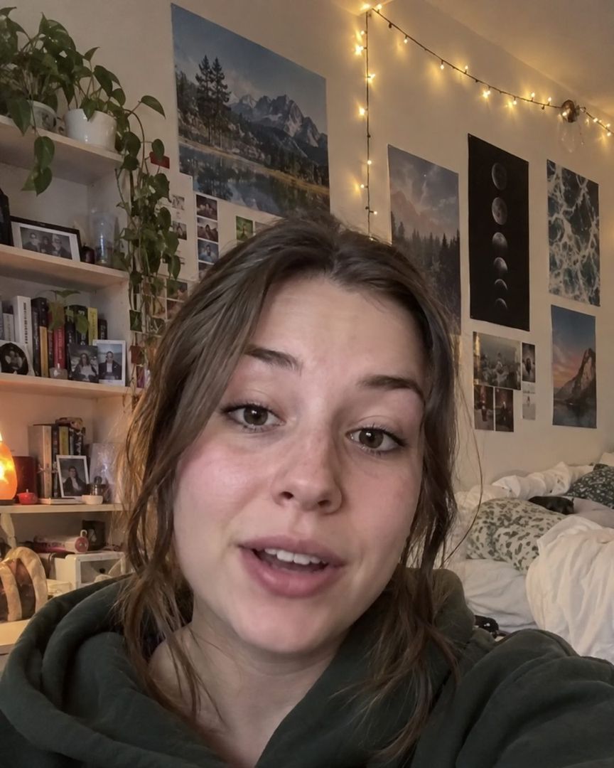 Original still: a phone-camera shot of one person talking to the lens in a cluttered bedroom, fairy lights and posters behind